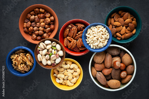 Variety of different types of nuts - almonds, pine nuts, pastachio, cashew, walnuts, pecan and hazelnuts- in bowls. Overhead view