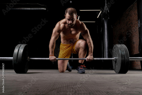 Strong weightlifter with muscular body prepares to lift the barbell