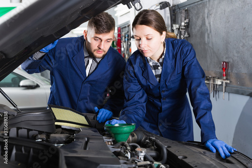 Two masters are replacing the oil in the car on workplace