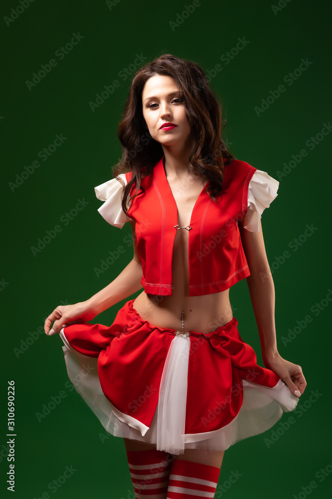 Concept woman at costume Christmas party. Full size portrait of an attractive beautiful brunette in a suit of Mrs. Santa Claus, striped golf with curly waves on a green isolated background Concept woman at costume Christmas party. Full size portrait of an attractive beautiful brunette in a suit of Mrs. Santa Claus, striped golf with curly waves on a green isolated background