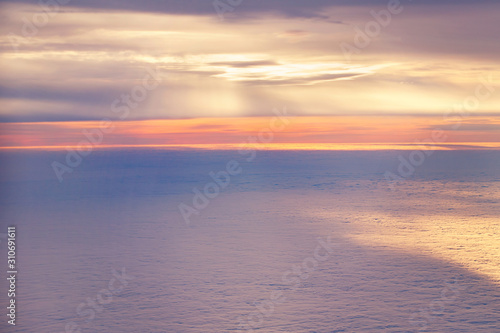 Aerial view from airplane of bright colorful pink red yellow orange sun beams in clouds on light blue sky at sunset sunrise. Evening or morning time nature. Natural background with copyspace.