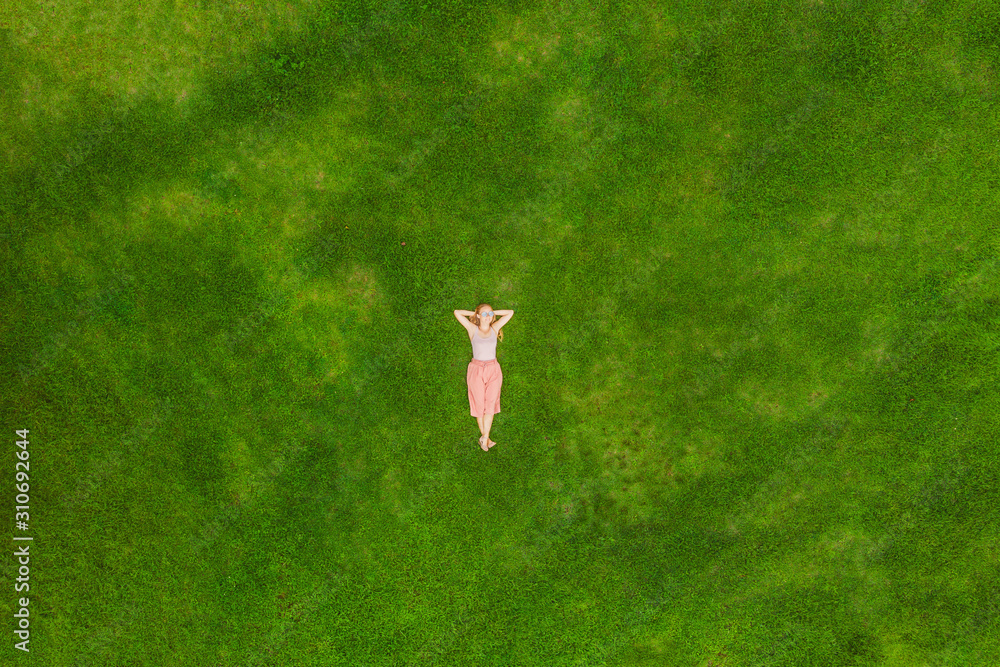 Young woman lying down in the middle of a field and relaxing, drone photo