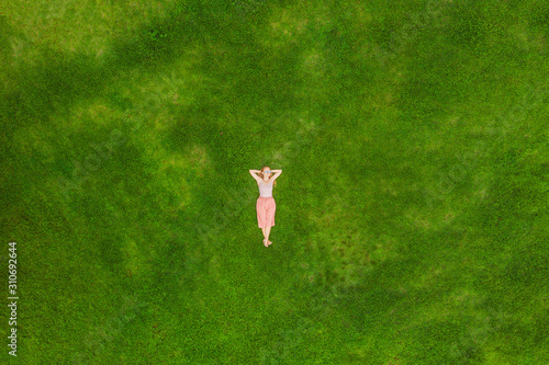 Obraz na płótnie Young woman lying down in the middle of a field and relaxing, drone photo w salonie