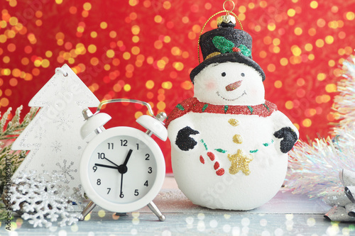 Christmas toy snowman, alarm clock, silver snowflake and tinsel on a red background. Yellow bokeh lights...