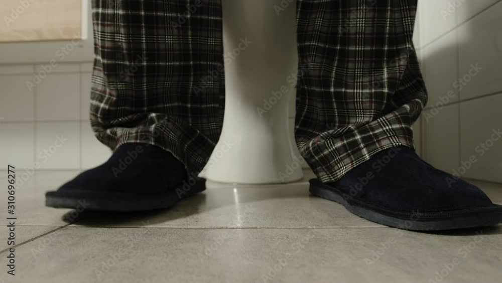 Male legs in a pajamas and slippers near a toilet - He takes down and up clothes Male legs in a pajamas and slippers near a toilet - He takes down and up clothes