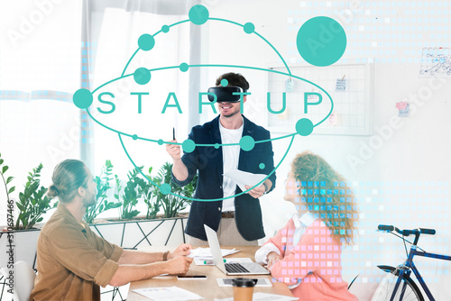 smiling businessman with vr headset in office near colleagues and startup illustration