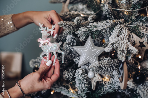 Cropped phoro of lady hands holding beautiful deer toy near the Christmas tree. New Year eve concept photo