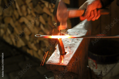 Ein Schmied bearbeitet mit seinem Hammer ein glühendes Stück Metall auf dem Amboss