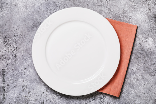 Empty ceramic plate of white color with a napkin on a gray concrete table, top view. Food background