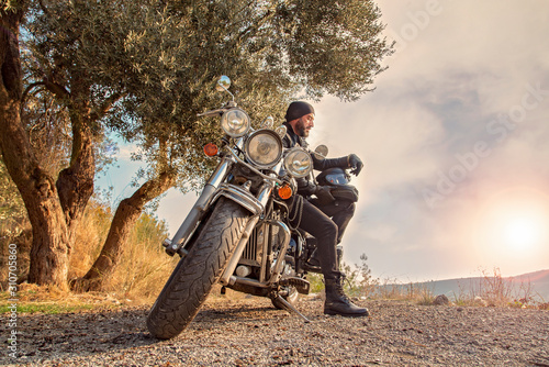Young Man with beard having rest in the countryside during motorbike trip.
