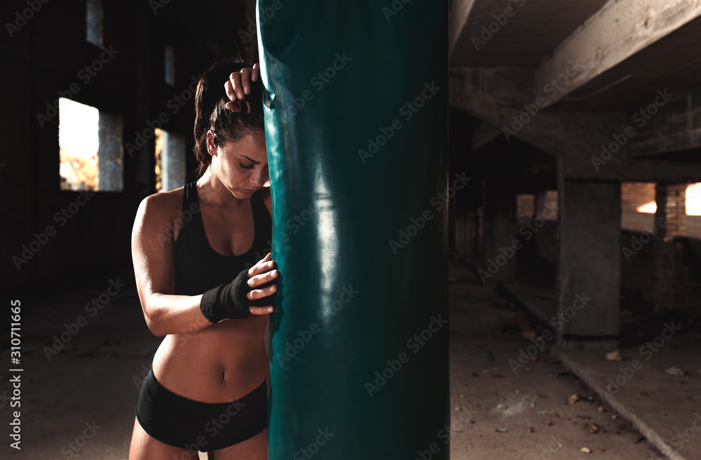 Female boxer resting after punching a boxing bag in warehouse.