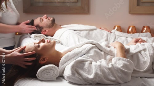 Beautiful couple lying down on massage beds enjoying a head massage in luxury spa. Relaxing and health.