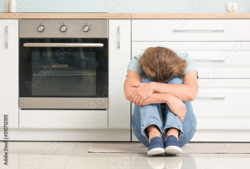 Depressed man in kitchen at...
