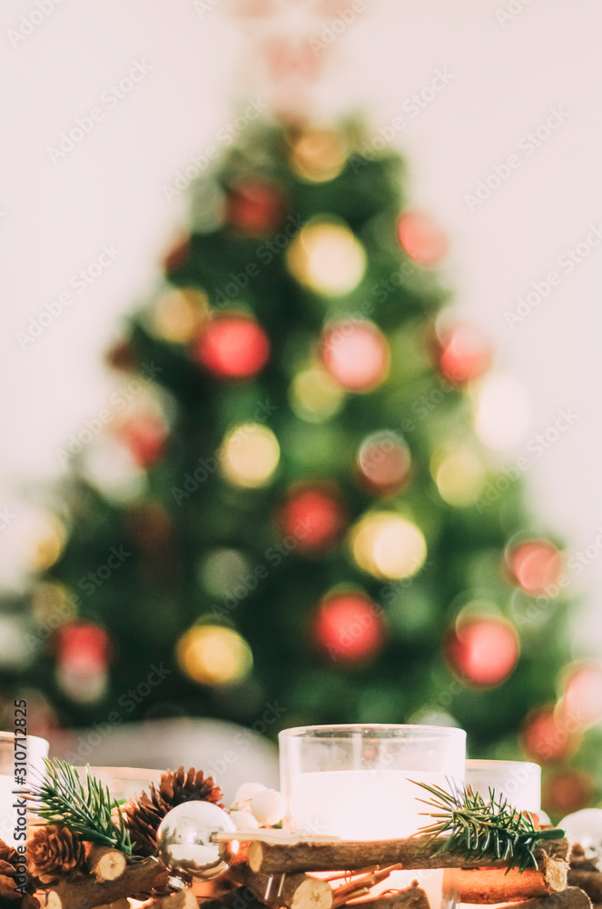 Christmas tree out of focus and on which its colorful ornaments stand out behind a beautiful wooden table centerpiece with Christmas candles - selective focus - Christmas tree out of focus and on which its colorful ornaments stand out behind a beautiful wooden table centerpiece with Christmas candles - selective focus -