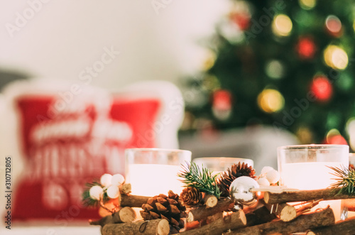 Nice Christmas tree decorated with different colored ornaments next to a cushion and a wooden centerpiece with candles with a beautiful Christmas design - selective focus - photo