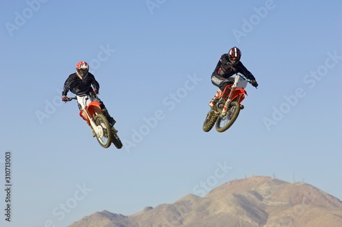 Motocross Racers Performing Stunt In Midair Against Blue Sky