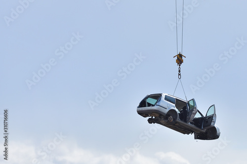 Discarded old car without wheels, lifted up by cables against a sky before recycling, with text space. The concept of car updates, consumption, old age, uselessness