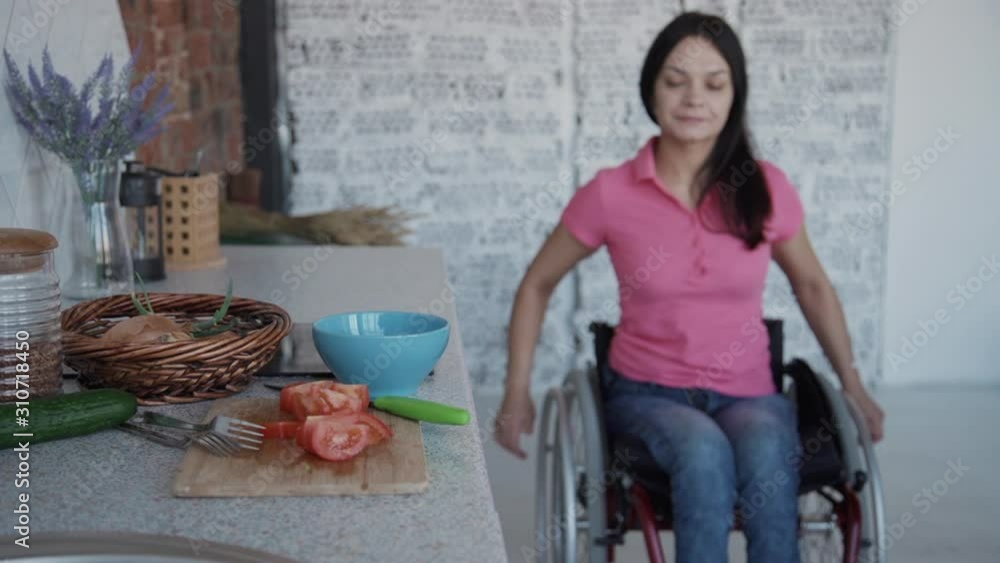 Young paraplegic woman in wheelchair riding to table with vegetable in
