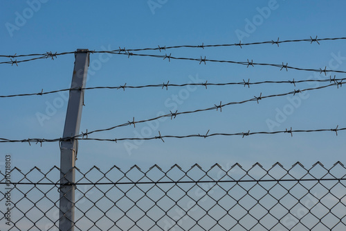Мetal fence with barbed wire. Clear blue sky as background. Protection, security concept.