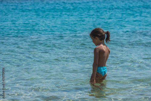 Sad little injured girl with bandage on her chin is standing at the water. No possibility to swimming or playing.