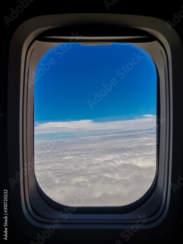 airplane window with a blue sky and white clouds