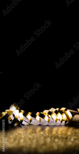 Golden ribbon on a vertical, black background with blurred, gold glitter. Christmas, new year, special occasions background, copy space.