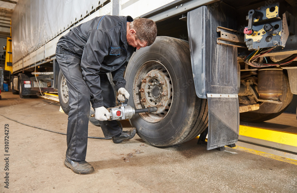 Truck repair service. Mechanic works with tire in truck workshop Truck repair service. Mechanic works with tire in truck workshop