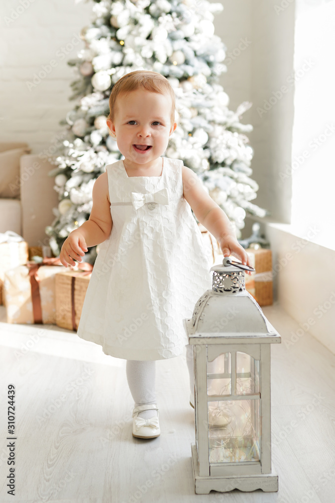 Fototapeta premium Happy small girl in white dress near christmas tree