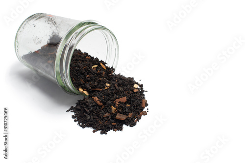 Dry leaves of black fruit tea with cinnamon and orange in a glass jar. Isolate on a white background.