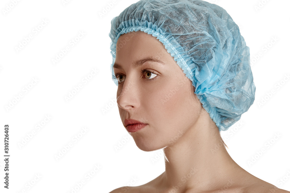 Beautiful girl in a medical cap of blue on a white isolated background. Beautiful young woman with clean fresh skin. Facial treatment. Cosmetology, beauty and spa. Skin care, close-up of the face Beautiful girl in a medical cap of blue on a white isolated background. Beautiful young woman with clean fresh skin. Facial treatment. Cosmetology, beauty and spa. Skin care, close-up of the face