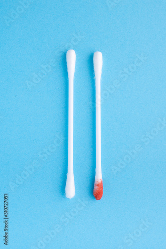 Blood on the hygiene cotton stick. Menstruation. Skincare mockup for design. Stack of disposable cotton stick on a blue background. Cosmetology concept. Bloody wound. Injury.