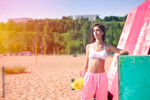 Portrait of teenager girl with skateboard in her hands. Sunny summer beach. Summer concept of extreme sport. Fun and leisure. Riding on scateboard.