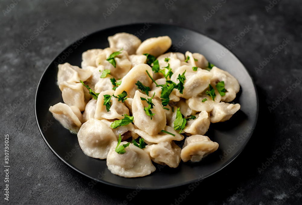 Dumplings - with spices and herbs in a black plate on a stone background. Traditional Russian dish - dumplings Dumplings - with spices and herbs in a black plate on a stone background. Traditional Russian dish - dumplings