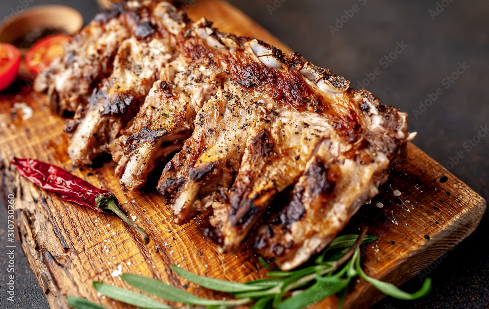 Grilled pork ribs with spices on a cutting board on a stone background Grilled pork ribs with spices on a cutting board on a stone background