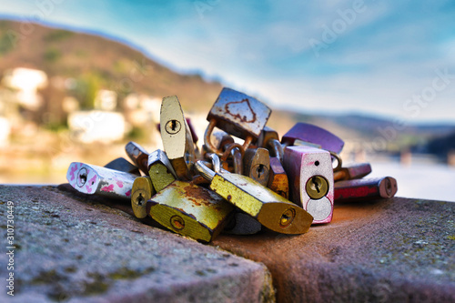 Bunch of love padlocks attached to old history bridge in city Heidelberg with blurry Odenwald forest and Neckar river in background