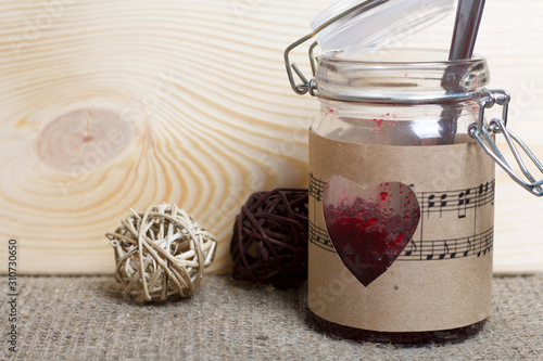 Glass jar of jam wrapped in paper with notes. Heart cut out in paper. Near rattan balls.