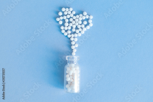 Heart made of homeopathic globules and glass bottle on blue background.  photo