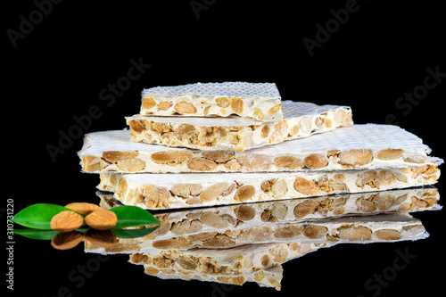 Traditional spanish sweet turron of white sweet base and almonds on the black reflective background. Christmas and New Year concept.
