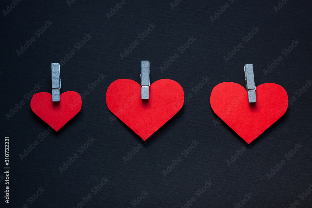 Three red hearts cut out of paper and wooden clothespins on a dark background. Three red hearts cut out of paper and wooden clothespins on a dark background.