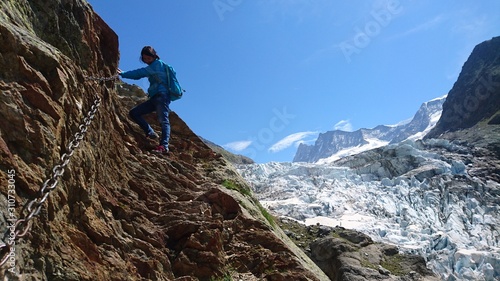 Alpine mountain climbing girl woman with backpack hard rocky hiking trail vista holding chains via ferrata swiss alps mountaineering with glaciers in the background