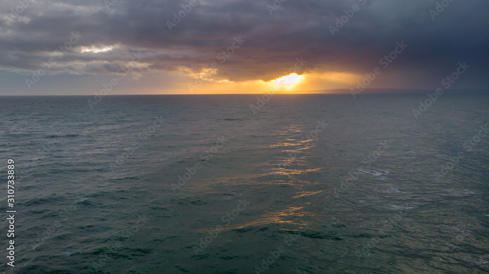 An aerial view of an sunset on choppy sea under a stormy cloudy black sky with ray of light from the sun behind it An aerial view of an sunset on choppy sea under a stormy cloudy black sky with ray of light from the sun behind it
