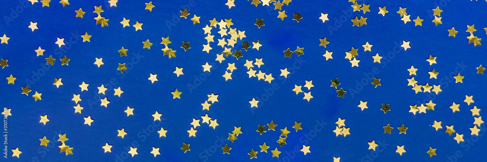 Delicate golden glitter star confetti on blue background. Creative banner and moody color of the picture. Delicate golden glitter star confetti on blue background. Creative banner and moody color of the picture.