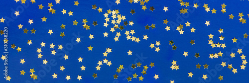 Delicate golden glitter star confetti on blue background. Creative banner and moody color of the picture.
