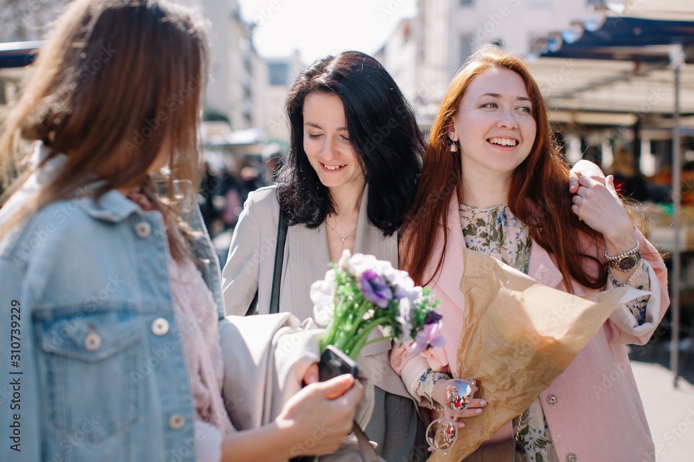 Three happy girlfriends walking by the street market in sunny day Three happy girlfriends walking by the street market in sunny day