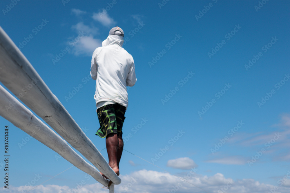 Man standing on a bamboo pole against a clear blue sky Man standing on a bamboo pole against a clear blue sky