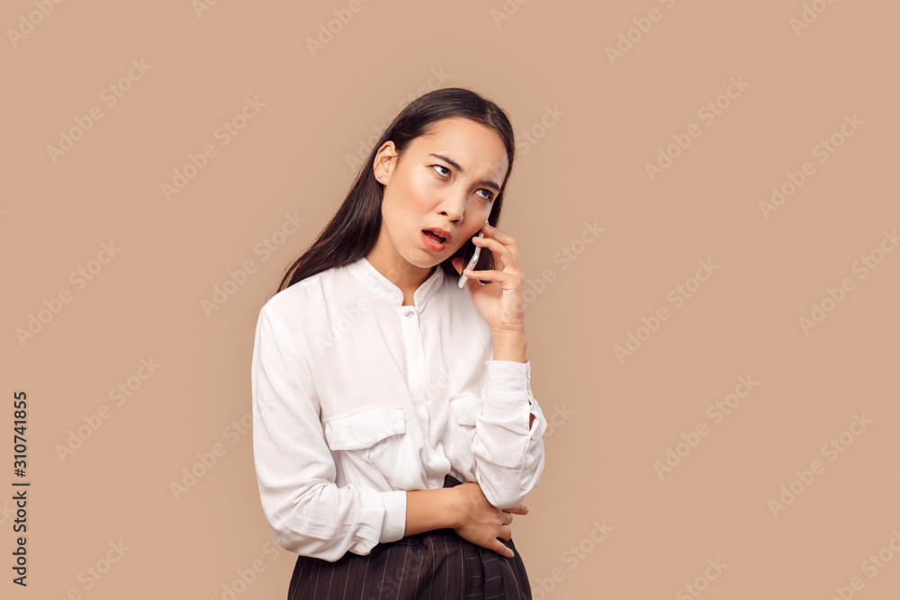 Freestyle. Young woman in shirt standing isolated on bage talking on smartphone grimacing bored Freestyle. Young woman in shirt standing isolated on bage talking on smartphone grimacing bored