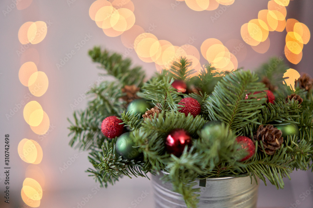 Small arrangement of fresh spruce in a metal pot. Christmas mood. Bokeh of Garland lights on background.