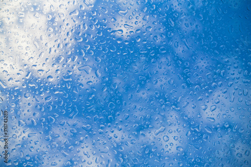 blue water drops background on glass amid blue sky with white clouds