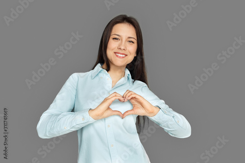 Freestyle. Young woman standing isolated on grey showing heart shape smiling cheerful © Viktoriia