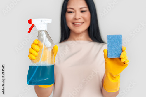 Freestyle. Asian woman in gloves standing isolated on white with spray and sponge close-up blurred background smiling happy